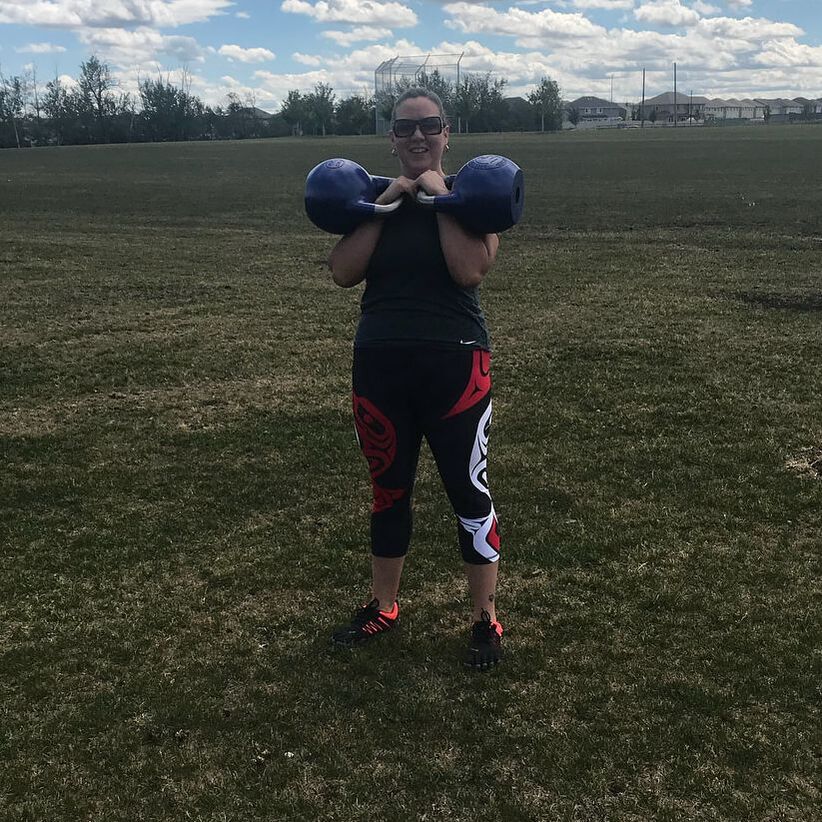 Tricia stands with kettlebells on a field.